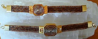 Twee armbanden met de band van gevlochten paardenhaar, in het midden een zilveren spiraal met gouden ondergrond.