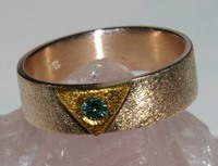 Een artistiek geheel: Een gematteerde 14 kt gouden band, met 24 kt gouden driehoek, die is ingelegd met een blauwe diamant. 